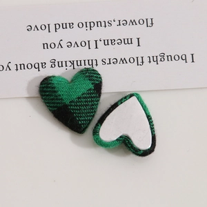 Macro detail of heart-shaped green tartan fabric patches with flat metal backing for DIY
