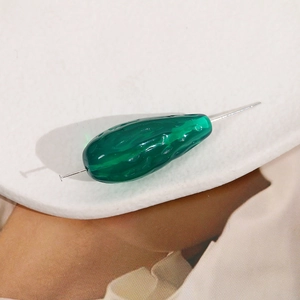 Detailed view of translucent green cucumber-shaped resin bead with piercing hole for DIY