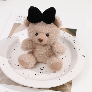 Soft curly plush bear doll with a black velvet bow on a decorative white polka dot plate