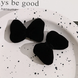 Close-up of a pair of plush black velvet bow hair clips on a decorative white tray