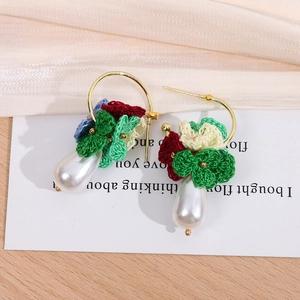 Detail handgestrickter Blumenohrringe mit weißer Tropfenperle auf einer Displaykarte