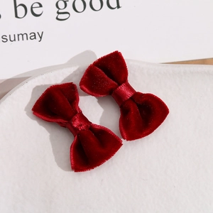 Detail of two handmade deep red velvet bow hair clips on a white ceramic plate