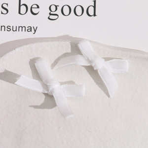 Close-up of two handmade white ribbon bows on a ceramic plate for DIY jewelry making