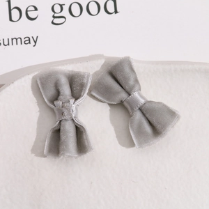 Close-up of two grey velvet handmade bow hair clips on a white textured ceramic tray