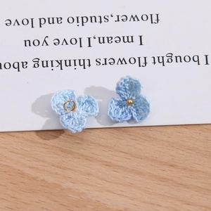 Detail von hellblauen gestrickten Blumen-Anhängern für DIY-Schmuck mit Goldperlen