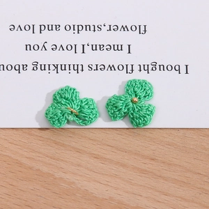 Detail von grün gestrickten Kleeblüten mit goldenen Ringen und Perlen auf Holzoberfläche