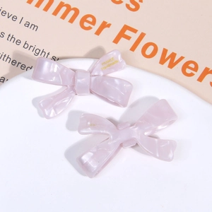 Detailed macro of pink acetate bow hair clips with marble texture and gold lettering