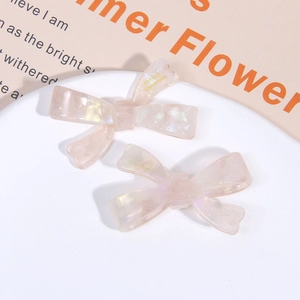 Detail of cream-colored acetate bow hair clips with a pearlescent finish and gold lettering