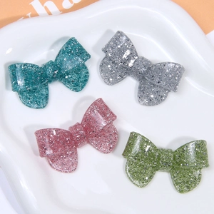 Close-up of glittery resin bow charms in blue, grey, purple and green for DIY crafts