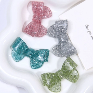 Detail of glittery resin bow accessories in pink, silver, blue and green on a white tray