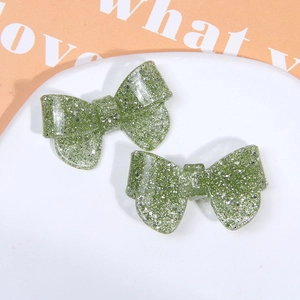Macro detail of grass green glitter bow hair clip on an oval white ceramic tray