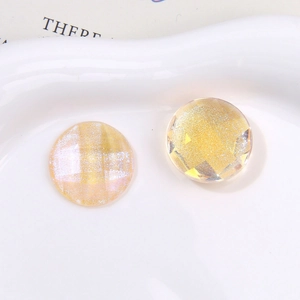 Close-up of Aurora iridescent multifaceted round yellow glitter charms on white ceramic