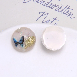 Detail von Harz-Charm mit blauem Schmetterling, goldener Rose und Glitzer auf flachem Boden