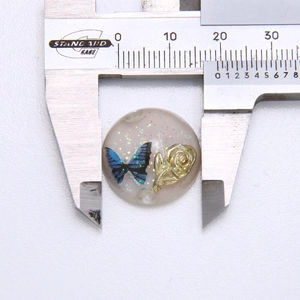 Detailansicht eines 20mm Harzperle mit Schmetterling und Goldrose neben einem Messschieber