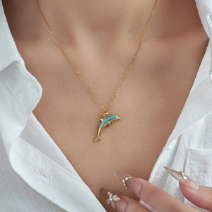 Collier pendentif dauphin doré avec émail bleu clair et cristaux blancs sur une femme
