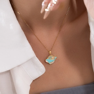 Close-up of a gold chain necklace with a blue enamel whale pendant on a female model