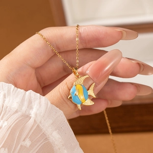 Handheld shot of a gold tropical fish necklace with blue and yellow enamel pendant details