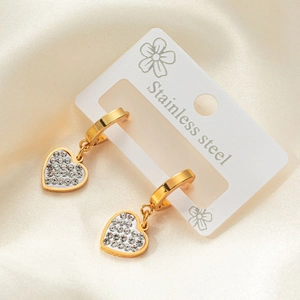Detalle de pendientes de corazón en acero dorado con cristales sobre fondo de seda blanca