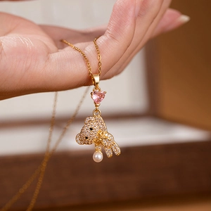 Detailed close-up of golden bear necklace with pink heart gem and elegant pearl pendant