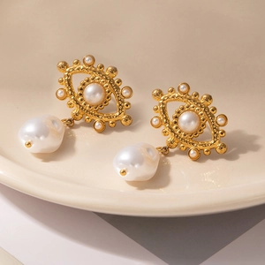 Detailed macro view of gold evil eye stud earrings with baroque pearls in a ceramic tray