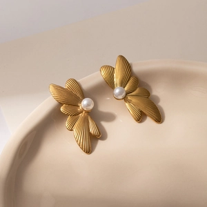 Elegant gold flower earrings with white pearls and striped metal petals on a ceramic tray