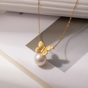 Detail of a brushed gold butterfly and white pearl pendant on a delicate chain necklace