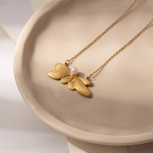 Detail of a golden wing pendant with a central pearl on a minimalist ceramic tray