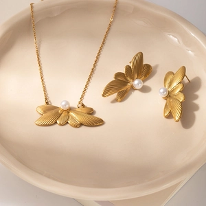 Close-up of golden wing-shaped jewelry set with white pearls in a ceramic tray