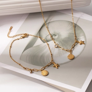 Dettaglio di bracciale e collana dorati con ciondoli a stella marina, conchiglia e zircone