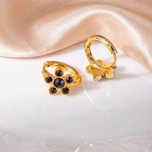 Dettaglio di orecchini a fiore dorati con zirconi neri su seta color champagne