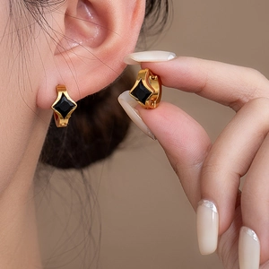 Detail of gold huggie earrings with black rhombus stone inlay and polished finish