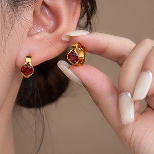 Detail of elegant gold hoop earrings featuring a vibrant red round-cut gemstone setting