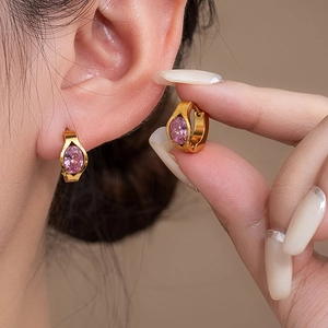 Macro shot of gold hoop earring with pink zircon stone on model's ear showing elegant details