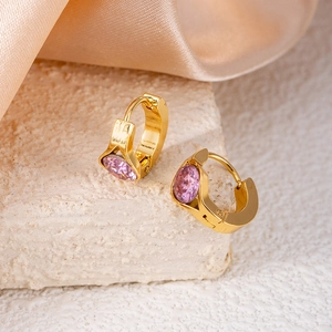 Detail of pink oval zircon huggie earrings in gold plated finish on white stone surface