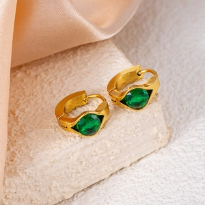 Close-up of gold huggie earrings featuring a green gemstone on a marble surface