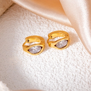 Close-up of gold brushed titanium steel earrings with oval zirconia on silk background