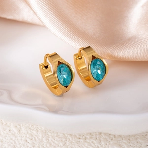 Detailed macro view of gold huggie earrings with oval blue rhinestones on silk fabric