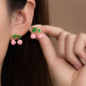 Primo piano di orecchini a lobo a ciliegia rosa con rami dorati su una modella
