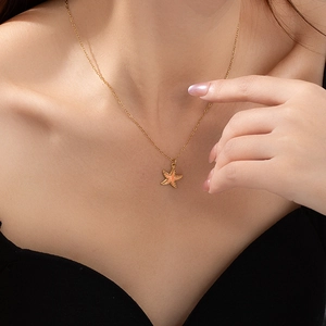 Detail van een fijne gouden ketting met een perzikkleurige zeester hanger op een model