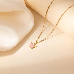 Detail van gouden ketting met roze kroonhanger op witte zijden stoffen achtergrond