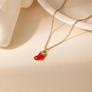 Détail d'un collier doré avec pendentif en forme de botte de Noël en émail rouge poli
