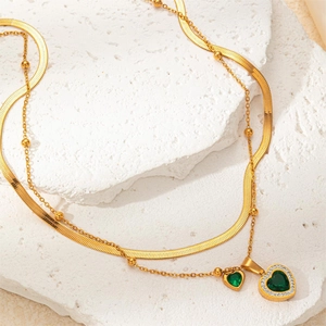 Detail of double-layered gold snake chain necklace with green heart-shaped crystal pendant