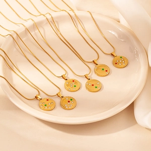 Detail of gold zodiac necklaces with small crystals on a ceramic plate with warm lighting