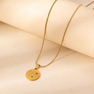 Gold stainless steel zodiac necklace with textured coin pendant on minimalist display stand