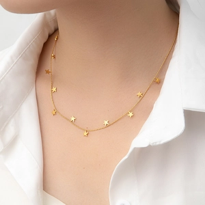Detailed view of delicate gold star charm necklace worn over a white minimalist shirt