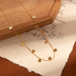 Detail of gold-plated stainless steel necklace with hollow rose floral charms on wood