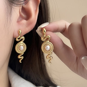 Detail eines schlangenförmigen Goldohrrings mit Perle, getragen von einem Modell