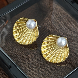 Detailaufnahme goldener Muschelohrringe mit Perle auf braunem Stoffhintergrund