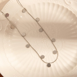 Close-up of a silver stainless steel chain with small hexagonal charms on a white ceramic plate