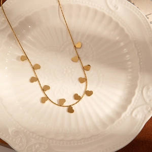 Detail of gold-plated necklace with tiny heart charms resting in a white ceramic bowl